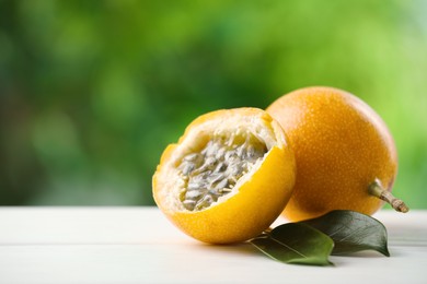 Photo of Ripe passion fruits and green leaves on white wooden table outdoors, closeup. Space for text