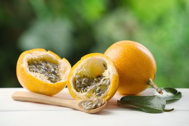 Photo of Ripe passion fruits, green leaves and seeds on white wooden table outdoors, closeup