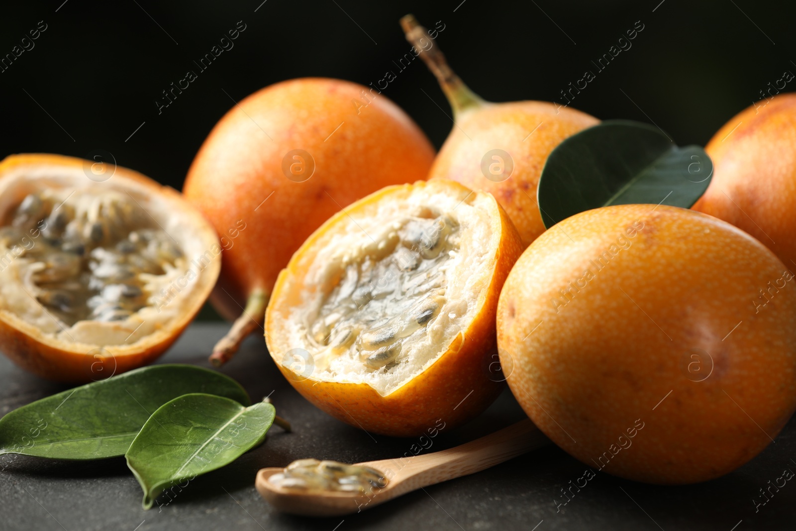 Ripe passion fruits, green leaves and seeds on black table, closeup Photo of Ripe passion fruits, green leaves and seeds on black table, closeup