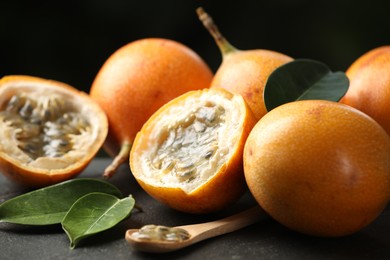 Photo of Ripe passion fruits, green leaves and seeds on black table, closeup