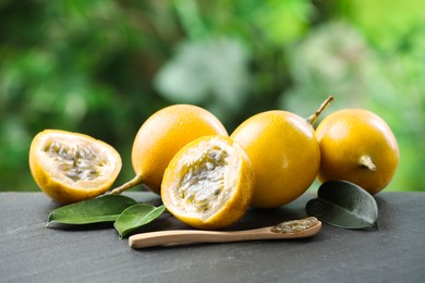 Photo of Ripe passion fruits, green leaves and seeds on black table outdoors