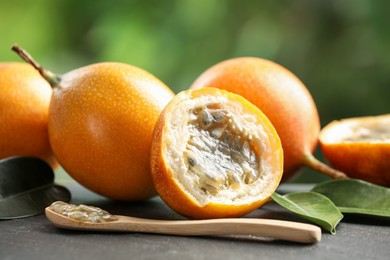 Photo of Ripe passion fruits, green leaves and seeds on black table outdoors, closeup