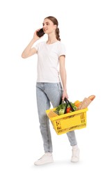 Photo of Woman with shopping basket full of products talking on phone against white background