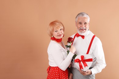 Photo of Lovely senior couple with gift box and rose on light brown background, space for text