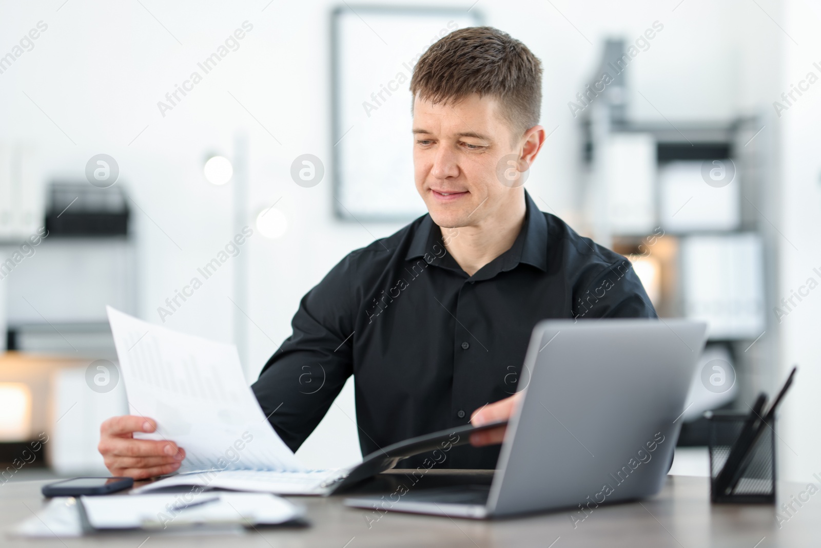 Photo of Handsome man working with documents at desk in office. Space for text