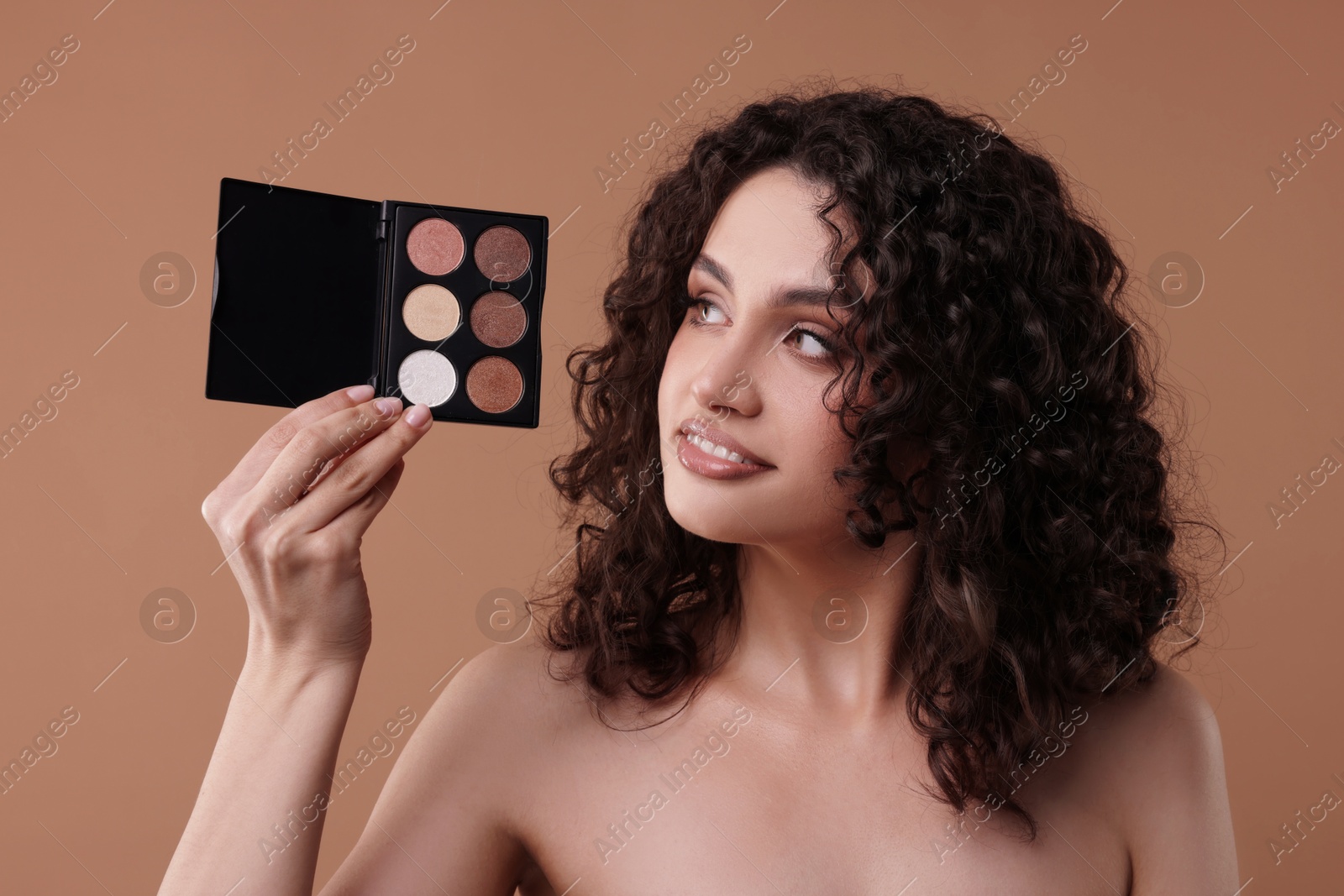 Smiling woman with eyeshadow palette on beige background Photo of Smiling woman with eyeshadow palette on beige background