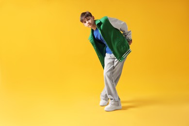 Photo of Boy in stylish clothes dancing on orange background, space for text