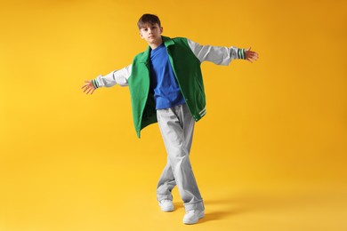 Photo of Boy in stylish clothes dancing on orange background