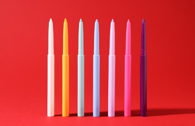 Photo of Colorful twist up eye pencils on red background, closeup
