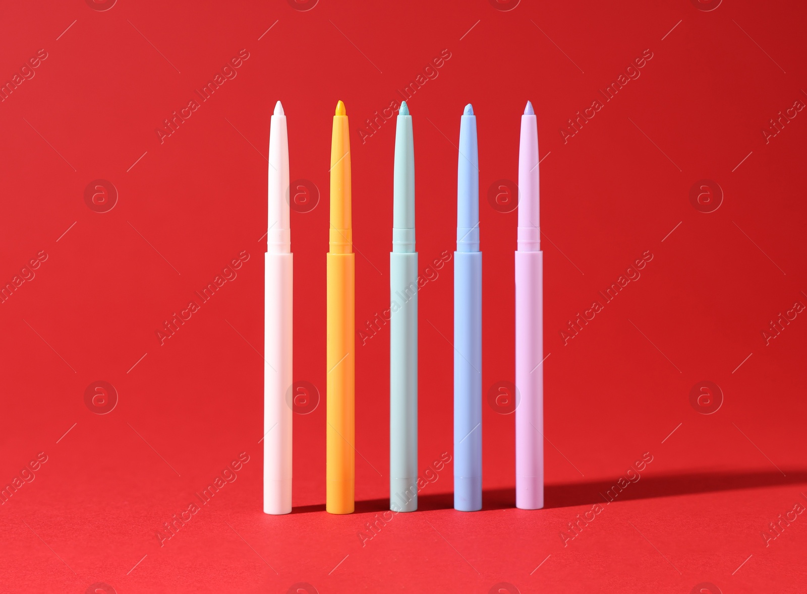 Colorful twist up eye pencils on red background, closeup Photo of Colorful twist up eye pencils on red background, closeup