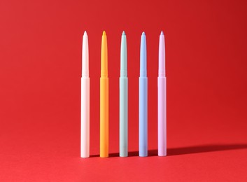 Photo of Colorful twist up eye pencils on red background, closeup