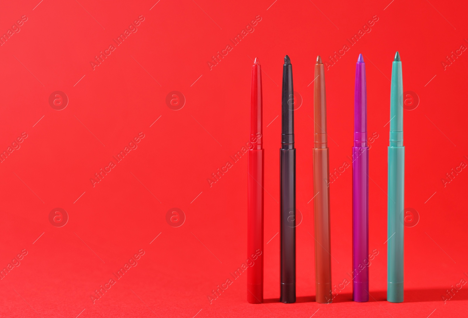 Colorful twist up eye pencils on red background, closeup. Space for text Photo of Colorful twist up eye pencils on red background, closeup. Space for text
