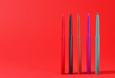 Photo of Colorful twist up eye pencils on red background, closeup. Space for text