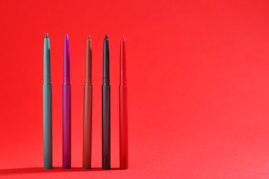 Photo of Colorful twist up eye pencils on red background, closeup. Space for text