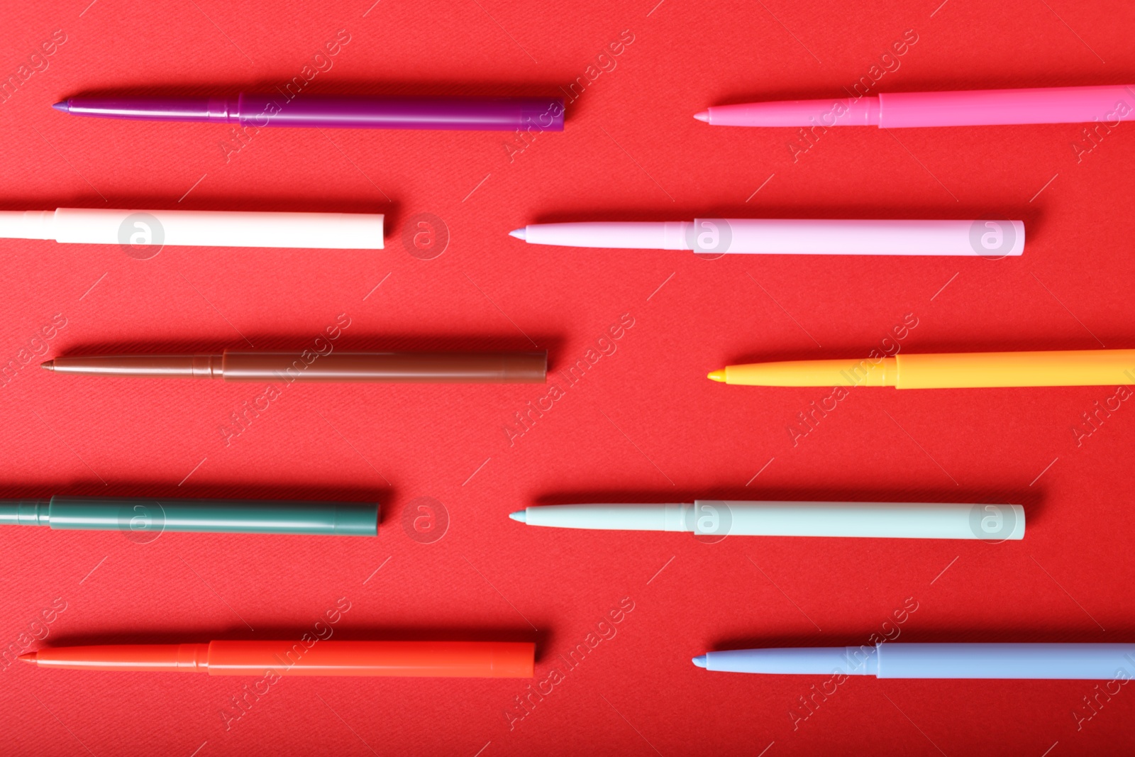 Colorful twist up eye pencils on red background, flat lay Photo of Colorful twist up eye pencils on red background, flat lay
