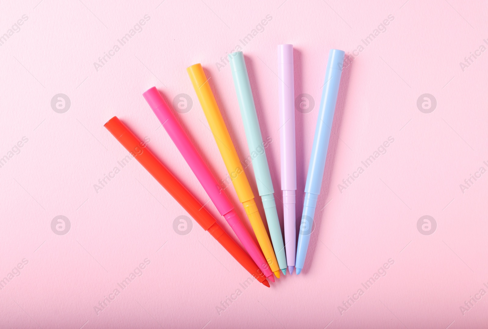 Colorful twist up eye pencils on pink background, flat lay Photo of Colorful twist up eye pencils on pink background, flat lay