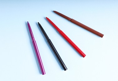 Photo of Colorful twist up eye pencils on light blue background, flat lay
