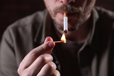 Photo of Man lighting cigarette with match on blurred background, closeup