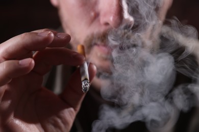 Photo of Man smoking cigarette on blurred background, closeup