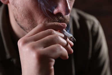 Photo of Man smoking cigarette on blurred background, closeup