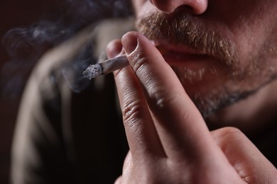 Photo of Man smoking cigarette on blurred background, closeup