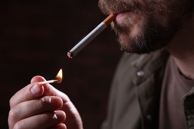 Photo of Man lighting cigarette with match on blurred background, closeup