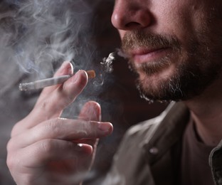 Photo of Man smoking cigarette on blurred background, closeup