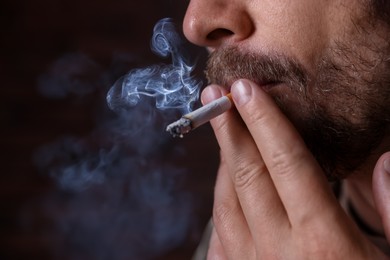 Photo of Man smoking cigarette on blurred background, closeup. Space for text