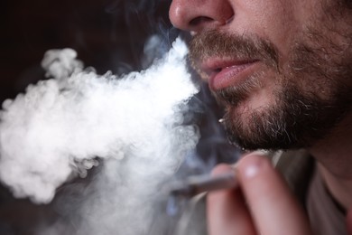 Photo of Man smoking cigarette on blurred background, closeup