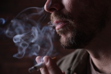 Photo of Man smoking cigarette on blurred background, closeup