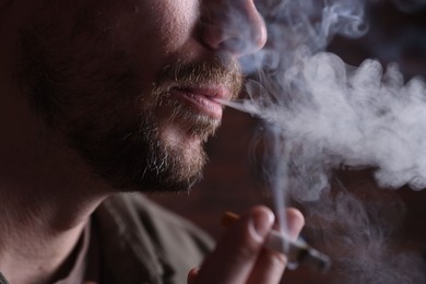 Photo of Man smoking cigarette on blurred background, closeup