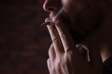 Photo of Man smoking cigarette on blurred background, closeup. Space for text