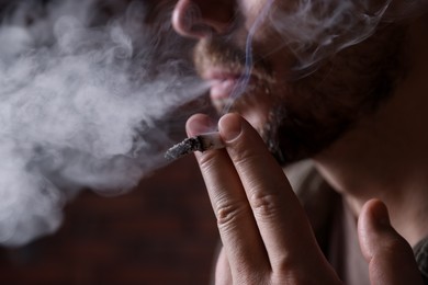 Photo of Man smoking cigarette on blurred background, closeup