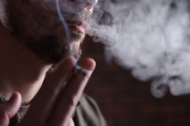 Photo of Man smoking cigarette on blurred background, closeup. Space for text