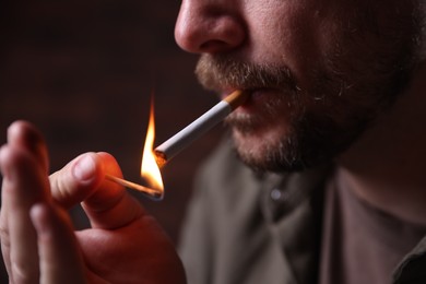 Photo of Man lighting cigarette with match on blurred background, closeup