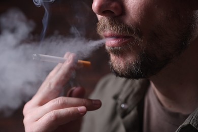 Photo of Man smoking cigarette on blurred background, closeup