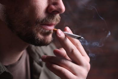 Photo of Man smoking cigarette on blurred background, closeup