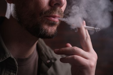 Photo of Man smoking cigarette on blurred background, closeup