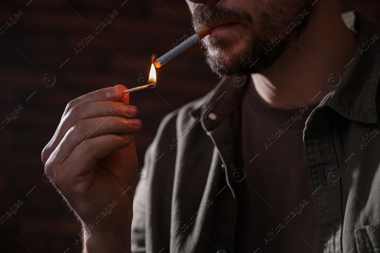 Man lighting cigarette with match on blurred background, closeup Photo of Man lighting cigarette with match on blurred background, closeup