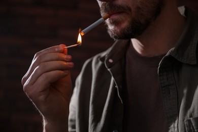 Photo of Man lighting cigarette with match on blurred background, closeup