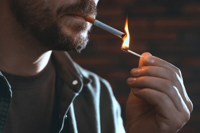 Photo of Man lighting cigarette with match on blurred background, closeup
