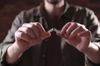 Photo of Man holding broken cigarette on blurred background, closeup. Stop smoking