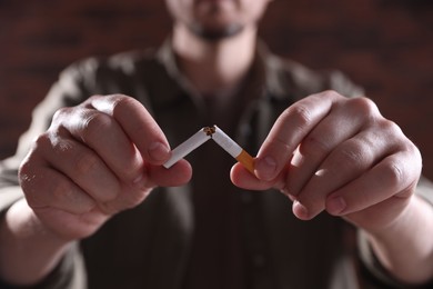 Photo of Man holding broken cigarette on blurred background, closeup. Stop smoking