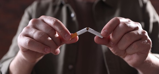 Photo of Man holding broken cigarette on blurred background, closeup. Stop smoking