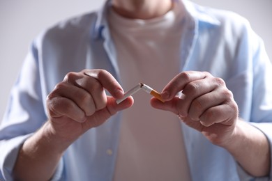 Photo of Man holding broken cigarette on light background, closeup. Stop smoking