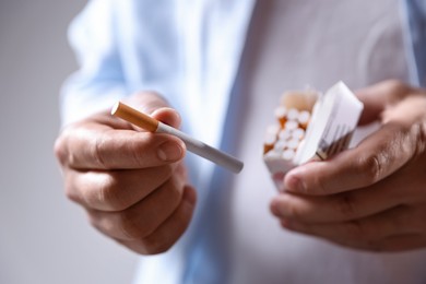 Photo of Man taking cigarette out of pack on light background, closeup. Smoking