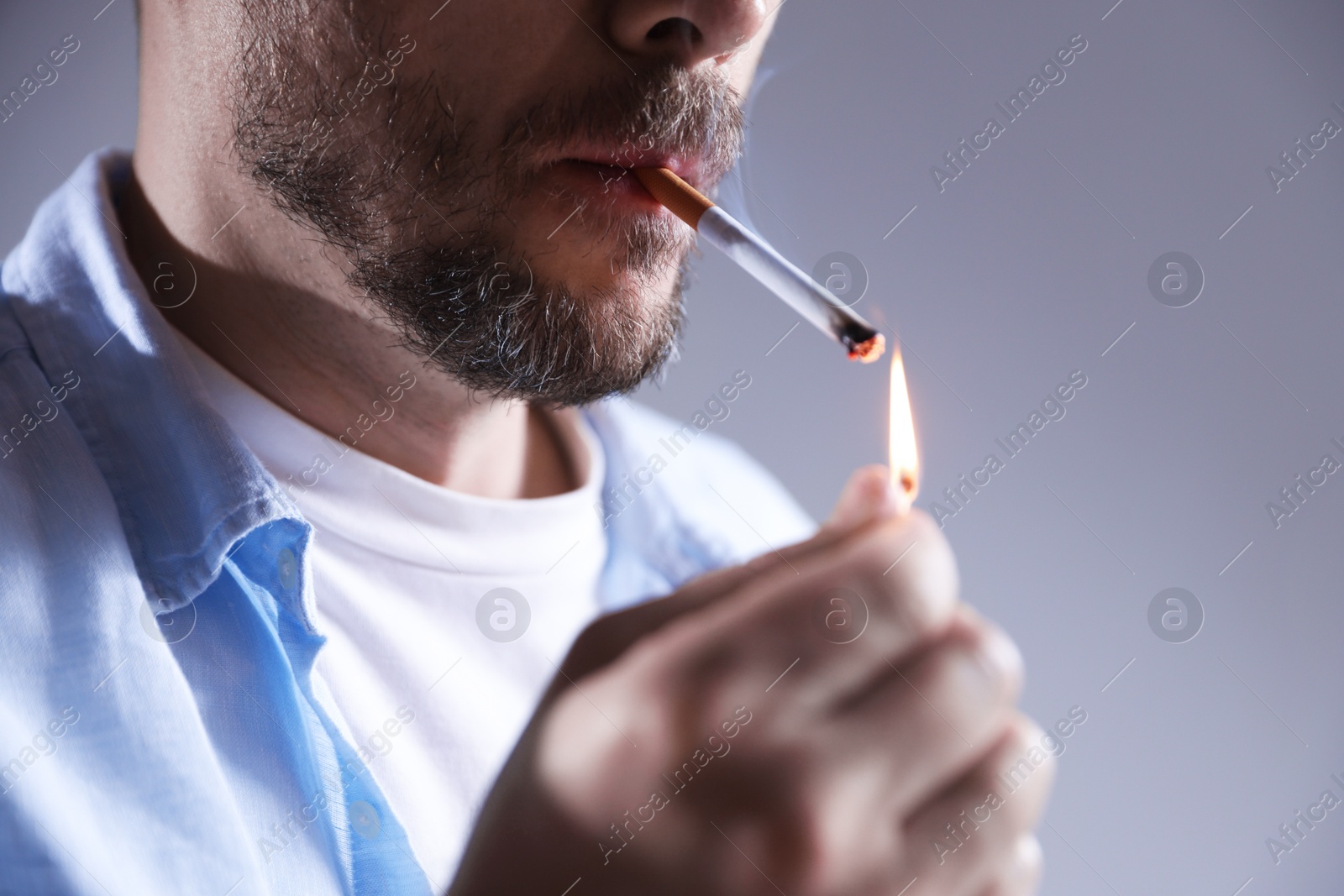 Man lighting cigarette with match on light background, closeup Photo of Man lighting cigarette with match on light background, closeup