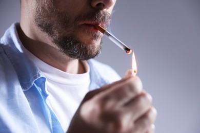 Photo of Man lighting cigarette with match on light background, closeup