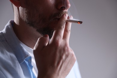 Photo of Man smoking cigarette on light background, closeup