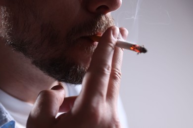 Photo of Man smoking cigarette on light background, closeup